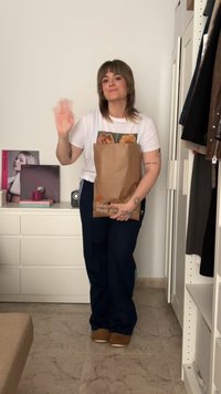 Bruine papieren tas met het opschrift "Love Wear me," versleten wit T-shirt met hondenprint, donkerblauwe sweatpants en lichtbruine instappers, staande binnen.