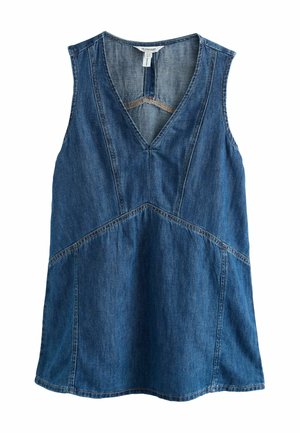 Kvinde iført ærmeløs denimtop og shorts, der holder en stor flettet taske med læderdetaljer.