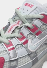 Άσπρο και ροζ αθλητικό παπούτσι Nike με ύφασμα από δίχτυ, γκρι κορδόνια και κείμενο «Bowerman Series» σε εσωτερική ετικέτα κοντά στη γλώσσα.