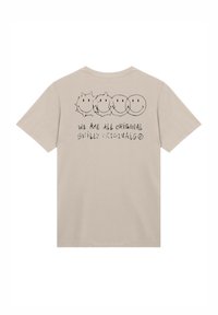 Beige T-shirt with short sleeves. The back features four smiley face graphics and text reading "WE ARE ALL ORIGINAL SMILEY ORIGINALS."