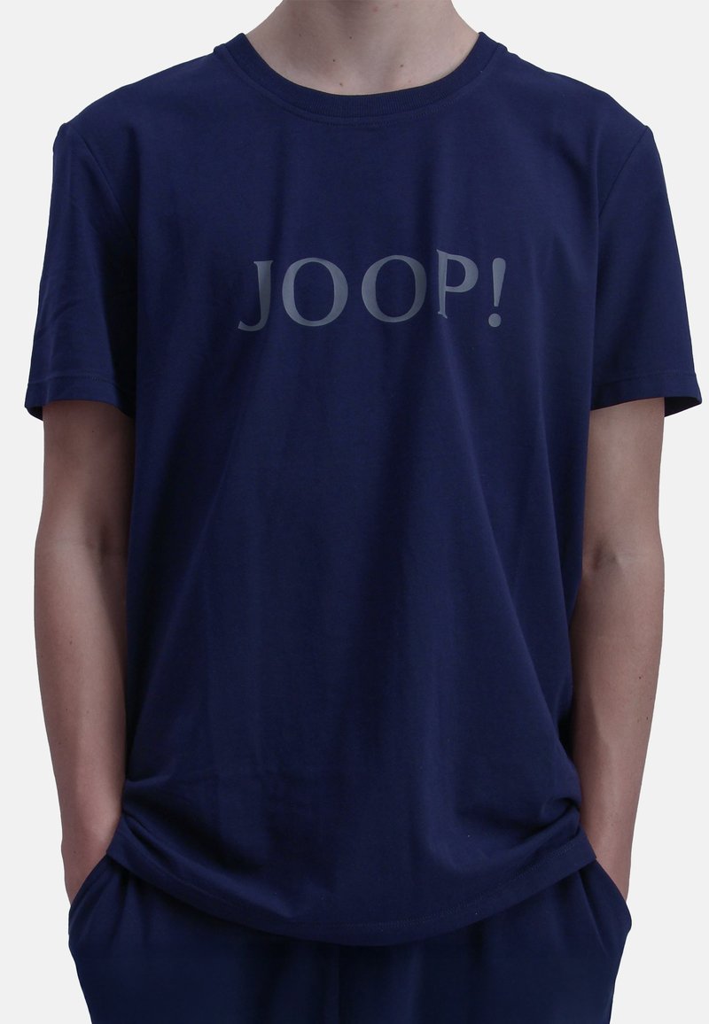Marineblaue Baumwoll-T-Shirt mit kurzen Ärmeln, das einen großen silbernen Druck von "JOOP!" über der Brust zeigt. Weicher Stoff und lockere Passform.