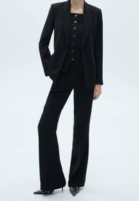 Černý podnikatelský oblek složený ze strukturovaného sáčka a přiléhavých kalhot, s vestou na knoflíky. Ostré černé lodičky s kovovými akcenty.
