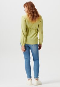 Maglietta lunga a maniche con texture verde chiaro e vita regolabile con cordino. Abbinata a jeans skinny blu chiaro e sneakers bianche.