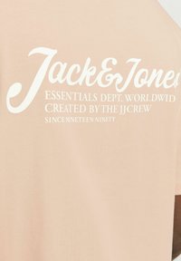 Lichtroze katoenen t-shirt met witte bedrukt tekst met de vermelding "Jack & Jones" en aanvullende merkdetails in variërende lettergroottes.