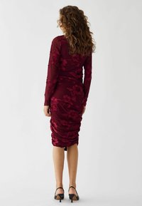 Burgunderfarbenes langärmliges Kleid mit floraler Spitzenüberlage, gerafften Details, figurbetontem Schnitt, knielangem Saum, kombiniert mit schwarzen High-Heel-Sandalen.
