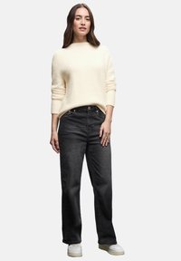 Cremefarbenes gestricktes Sweatshirt mit Rundhalsausschnitt, kombiniert mit schwarzen High-Waist-Jeans und weißen Sneakers. Schlichtes Design, lockere Passform.