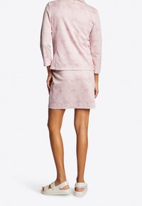 Abito rosa chiaro con fantasia, composto da una blusa a tre quarti e una gonna aderente. Il tessuto presenta un design testurizzato. Indossato con sandali leggeri.