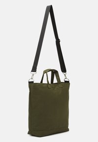 Sac fourre-tout vert olive avec double poignées, bandoulière noire ajustable, tissu durable et design minimaliste. Dispose d'accents de quincaillerie argentée.