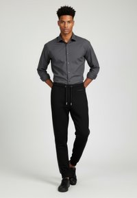 Grå skjorte med lange ærmer, parret med sorte sweatpants med sidelommer og snor i taljen. Sorte sneakers fuldender looket.