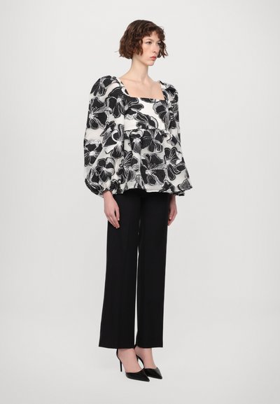 Top de flores en blanco y negro con manga abullonada y escote cuadrado, combinado con pantalones de pierna ancha negros y tacones puntiagudos. Textura de tela suave.