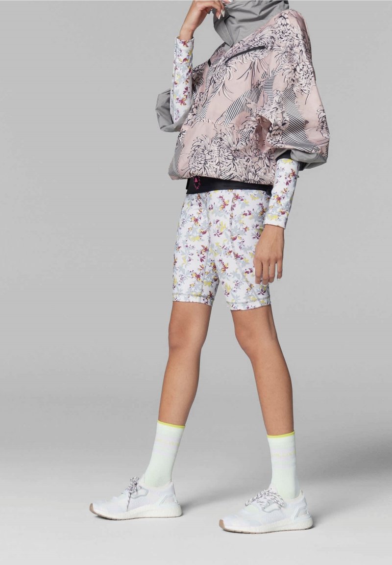 Top a maniche lunghe con motivo floreale nei toni del rosa e del grigio, abbinato a pantaloni corti floreali coordinati. Sneakers bianche con dettagli grigi e calzini gialli.