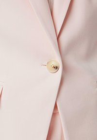 Blazer rosa chiaro in tessuto dalla superficie liscia, con un bottone circolare crema al centro e un colletto sagomato.