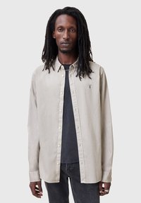  Lichtbeige lange mouwen knoopshirt met een klassieke kraag, twee voorzakken en een subtiele logodetail op de borst. Vlakke textuur.