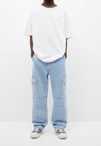 Camiseta blanca oversize, pantalones cargo azul claro con bolsillos laterales y zapatillas azules y blancas. Diseño simple, corte relajado, textura suave.