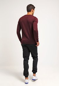 Bordeauxfarbenes Langarm-Sweatshirt mit taillierter Form, kombiniert mit schwarzen schmal zulaufenden Hosen. Verfügt über gerippte Bündchen und einen schlichten Rundhalsausschnitt.