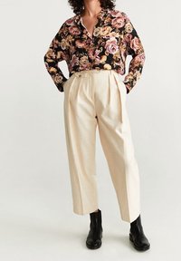 Blusa nera a fiori con fiori rosa e gialli, abbinata a pantaloni beige a pieghe e stivali neri alla caviglia. Tessuto morbido, vestibilità rilassata.