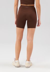 Brown active shorts with a high waistband, smooth texture, and stitched detailing, paired with light-colored athletic shoes.