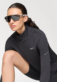 Sort langærmet træningsbluse med høj krave og struktureret stof, der har et lille hvidt Nike-logo på brystet og detaljer på ærmerne.
