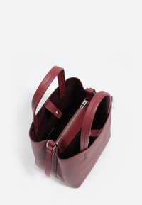 Mała bordowa skórzana torebka z dwoma uchwytami i centralną komorą zamykaną na zamek, otwartą u góry, ukazującą wnętrze.