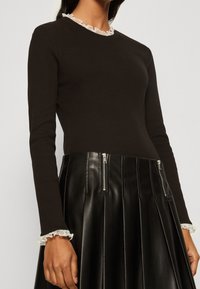 Svart ribbad långärmad topp med en vit volangkrage, kombinerad med en svart läderkjol med dragkedjor och veckad design.
