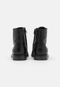 Botas de cuero negro hasta el tobillo con cremalleras verticales en la parte posterior, punteras redondas y tacones apilados. Textura suave con un sutil detalle de grano.