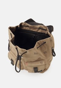 Borsa in canvas marrone con dettagli neri, chiusura a coulisse, fodera interna e tasca esterna con motivi a logo. Vista dall'alto aperta.