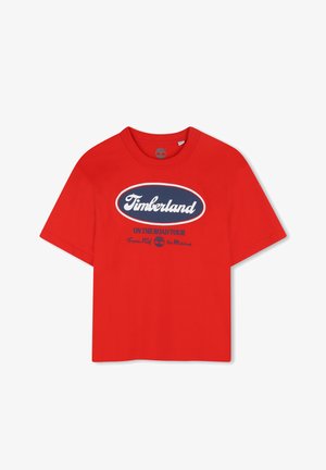 T-shirt rossa in cotone con maniche corte e scollo a girocollo. Presenta un logo circolare Timberland blu e bianco con testo "ON THE ROAD TOUR."