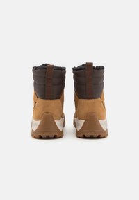 Bottines en daim marron et en tissu sombre avec une semelle texturée, des cols rembourrés et des languettes en boucle à l'arrière pour un enfilage facile.