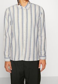 Camisa de botones de manga larga a rayas en una tela ligera, con rayas verticales en azul y gris, con un collar clásico y puños abotonados.