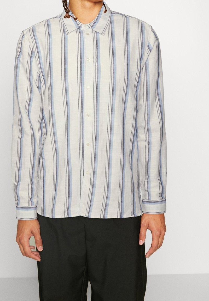 Camisa de botones de manga larga a rayas en una tela ligera, con rayas verticales en azul y gris, con un collar clásico y puños abotonados.