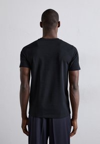 Czarna, krótka koszulka z krótkim rękawem, z klasycznym okrągłym dekoltem i gładką fakturą, oglądana z tyłu, z prostym krojem i bez widocznych logo.