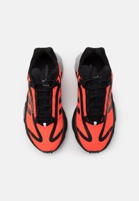 Sportovní boty s jasně oranžovým svrškem s černými akcenty, šněrovacím designem, texturovanou podrážkou a logem na jazyku.