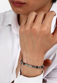 Metalarmband med växlande glansiga svarta pärlor och glänsande silversegment, med en liten gyllene accent i mitten.