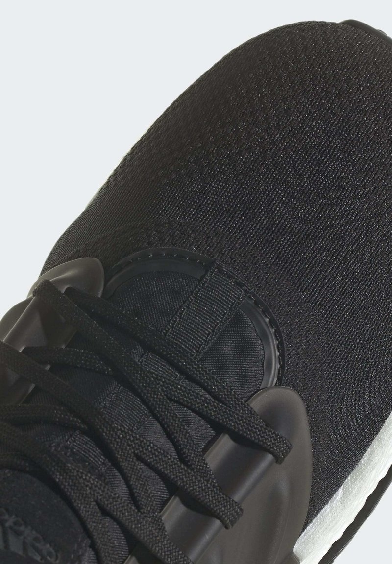Schwarzer Sportschuh mit Obermaterial aus strukturiertem Stoff, auffälligem Schnürsystem und einer gepolsterten weißen Zwischensohle in schlanker, konischer Form.