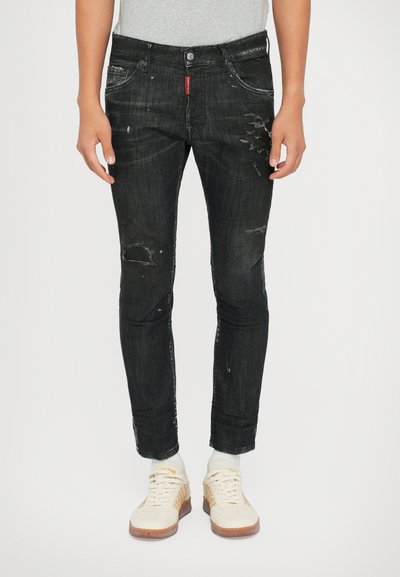 Sorte denim jeans med slim fit, prydet med slidte detaljer og falmede områder, parret med hvide sneakers og lyse sokker.