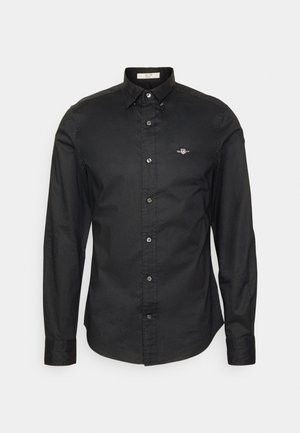 Sort skjorte med lange ærmer, lavet af bomuld, med et lille broderet logo på brystet og sølvknapper.