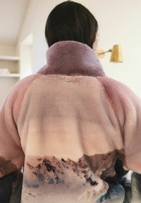 Fleece jacket featuring a gradient of soft pink, purple, and grey hues with a high collar and subtle mountain pattern details.