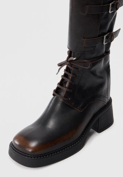 Brown leather ankle boot with a rounded toe, lace-up front, and buckle accents on the upper. Features a chunky block heel and textured finish.