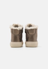 Botas altas marrones con un suave forro crema, fijadas con correas laterales y con una suela de goma texturizada.