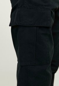 I pantaloni cargo neri presentano una tasca laterale, realizzati in materiale robusto con una texture liscia e cuciture rinforzate per garantire durata.