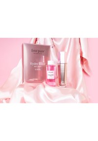 Hydro Elixir hudplejesæt med pink mist sprayflaske, klar glasserum i sølvaccentueret emballage og en pink satinbaggrund.