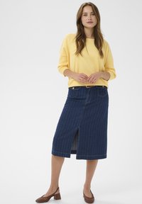 Pull en tricot jaune à manches larges associé à une jupe en denim longueur genou avec une fente à l'avant, un motif à fines rayures et des poches latérales.