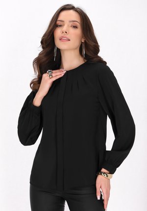 Blusa nera con scollatura rotonda, maniche lunghe a sbuffo e dettagli plissettati. Tessuto liscio e vestibilità rilassata, abbinata a leggings neri.