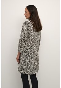 Robe ample avec une base crème et un motif à pois noirs, dotée de manches trois-quarts et d'une coupe droite.