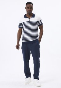 Gestreepte polo in wit en marineblauw, met korte mouwen en een kraag. Gepaard met losse marineblauwe broeken en witte sneakers.