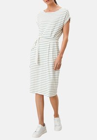 Weiß gestreiftes Kleid mit kurzen Ärmeln und einem Bindegürtel; hat Seitentaschen und wird mit weißen Sneakers für einen lässigen Look kombiniert.