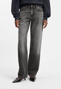 Höga, vida jeans i blekt svart denim med fem knappstängning och subtila slitningsmönster. Kombinerade med spetsiga svarta klackskor.