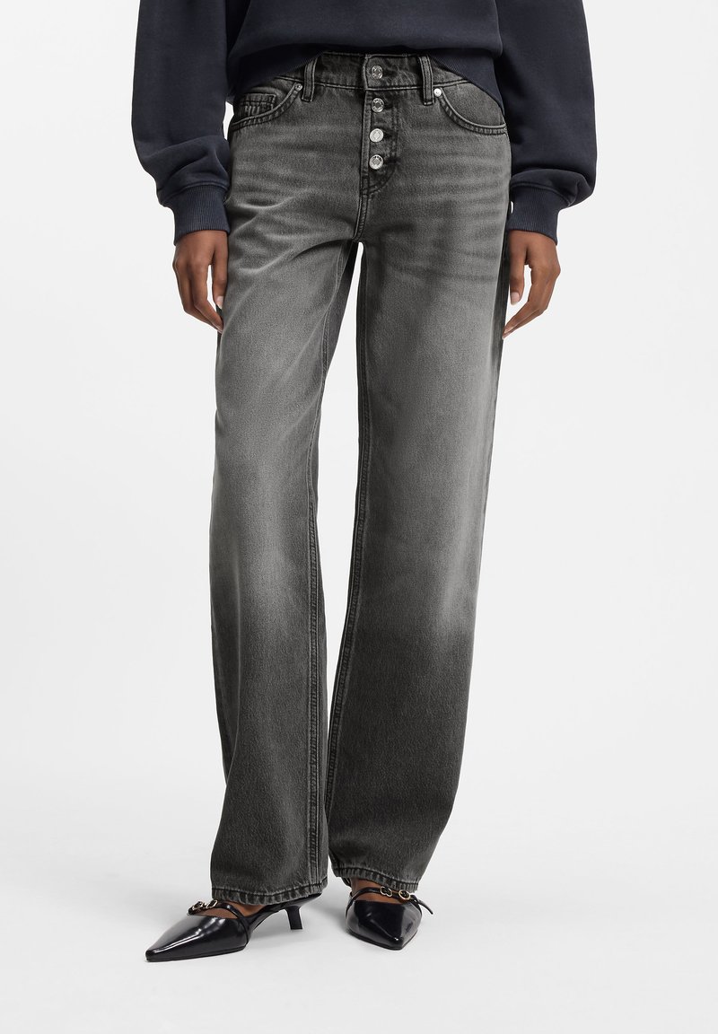 Höga, vida jeans i blekt svart denim med fem knappstängning och subtila slitningsmönster. Kombinerade med spetsiga svarta klackskor.