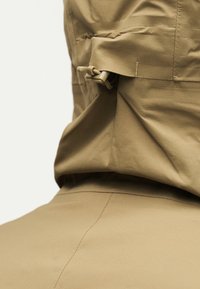 Šviesiai rudos spalvos švarko gobtuvas su reguliuojamu raišteliu ir užsegimu su spaustuku, matomas iš nugaros.