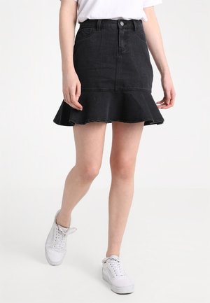 Black denim skirt with a flared hem, featuring a button closure and front pockets. Worn with a white shirt and white sneakers.